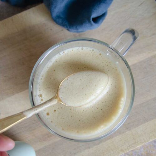Spoon with froth over clear mug on cutting board