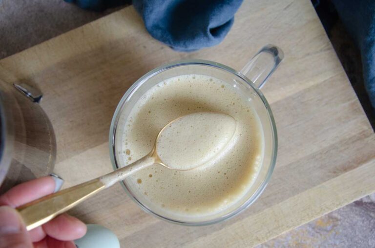 Spoon with froth over clear mug on cutting board