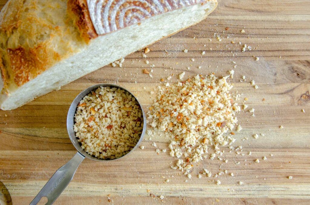 Bread crumbs in measuring cup beside sourdough loaf