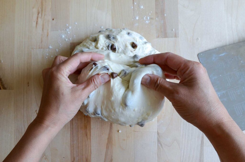 Hands pinching sourdough chocolate chip croissant dough