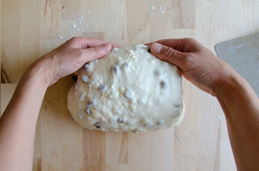 Hands folding dough under on wood board