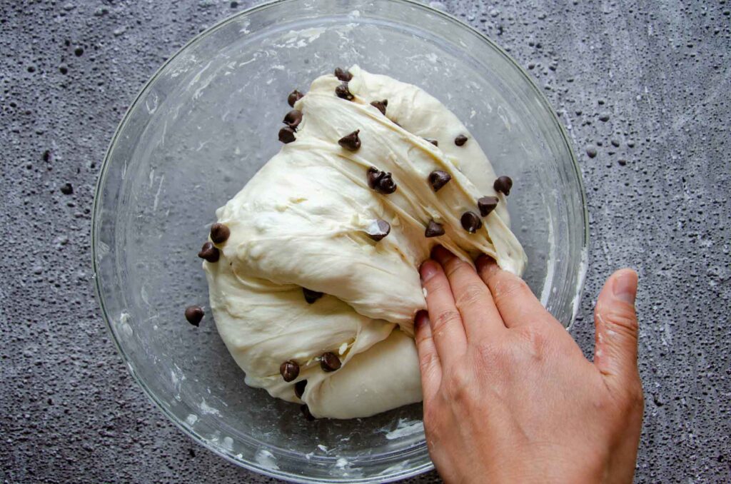 Hand folding chocolate chips into croissant dough