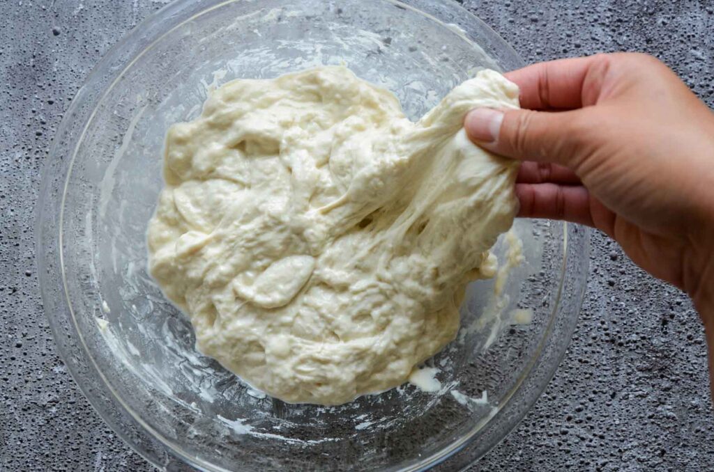 Hand stretching dough in glass bowl