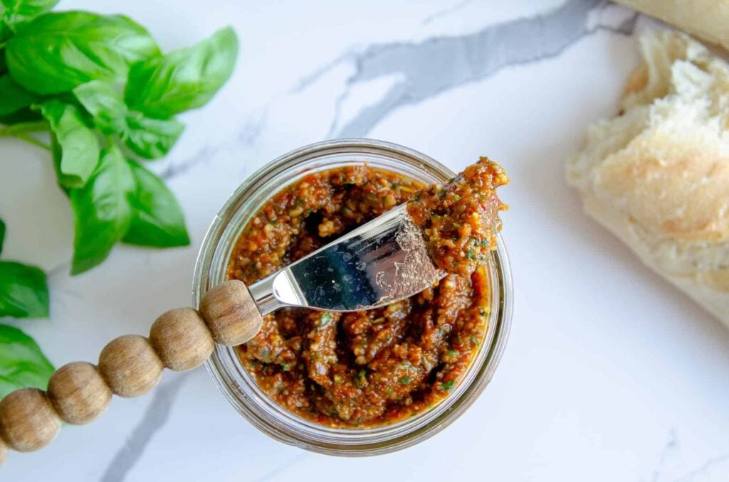 wooden knife with tomato pesto resting on jar