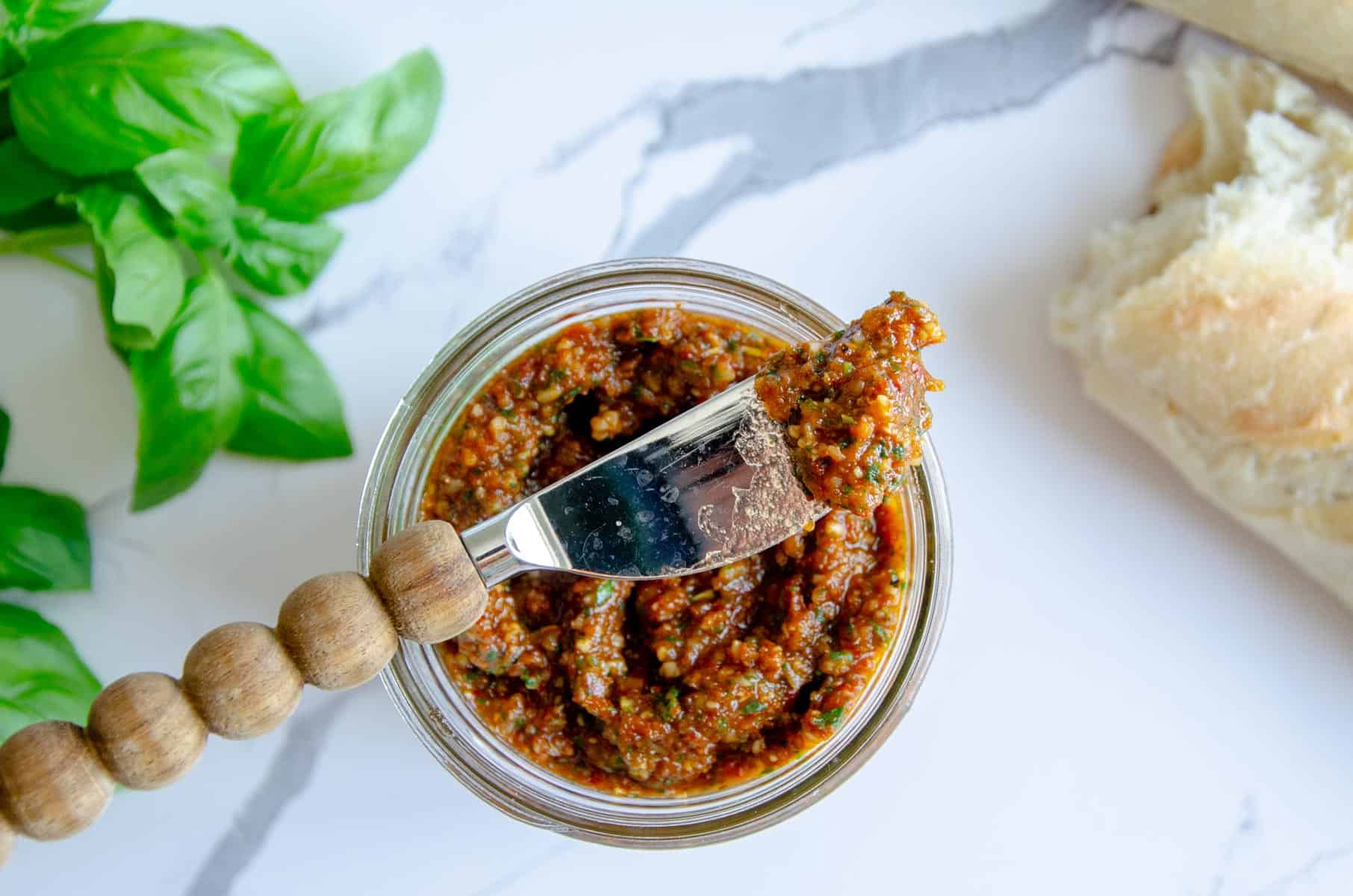 wooden knife with tomato pesto resting on jar