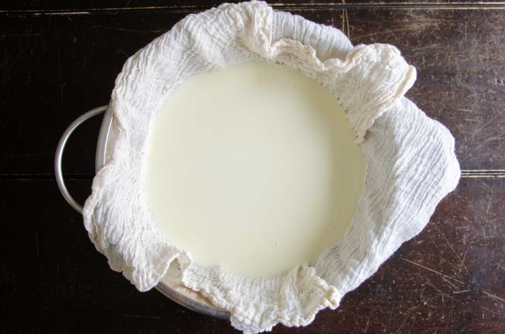 homemade Greek yogurt in a cloth lined strainer over a bowl