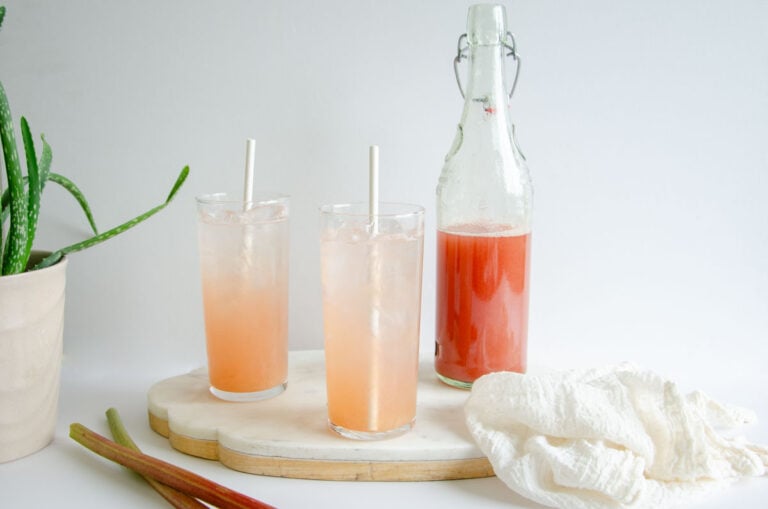 rhubarb syrup in a bottle with two glasses of water and syrup next to it