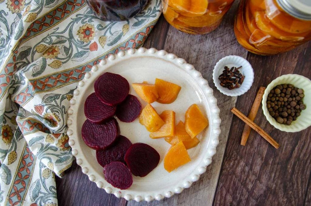 golden pickled beets and red pickled beets on a plate with spices and jars of pickled beets all around