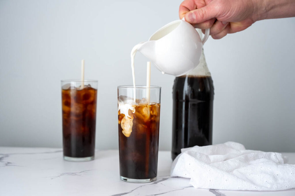 pouring cream into a tall glass of cold brew concentrate
