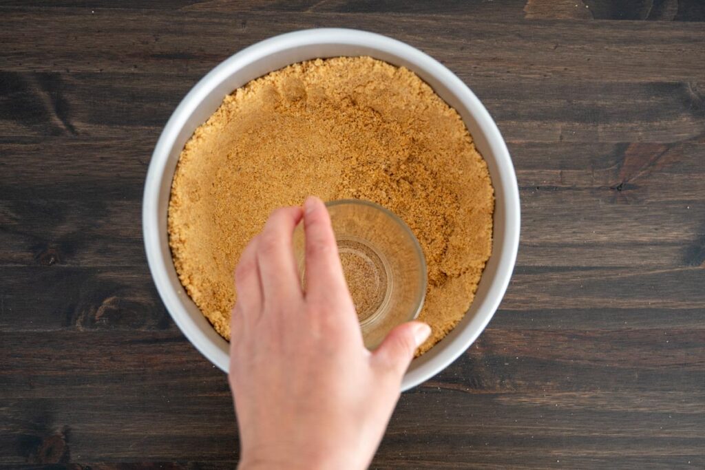 pressing graham cracker crust into pan using a glass