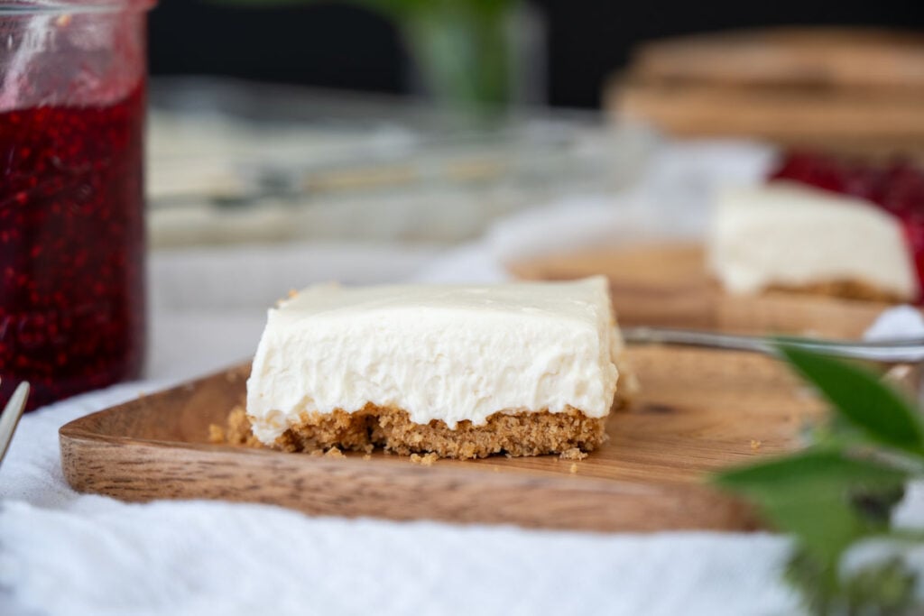 a piece of no bake cheesecake on a wood plate with raspberry jam in the background