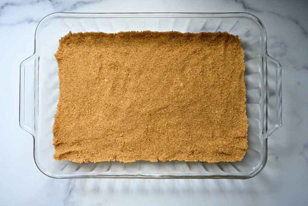 pressing graham cracker crust for no bake cheesecake in a 9x13 cake pan