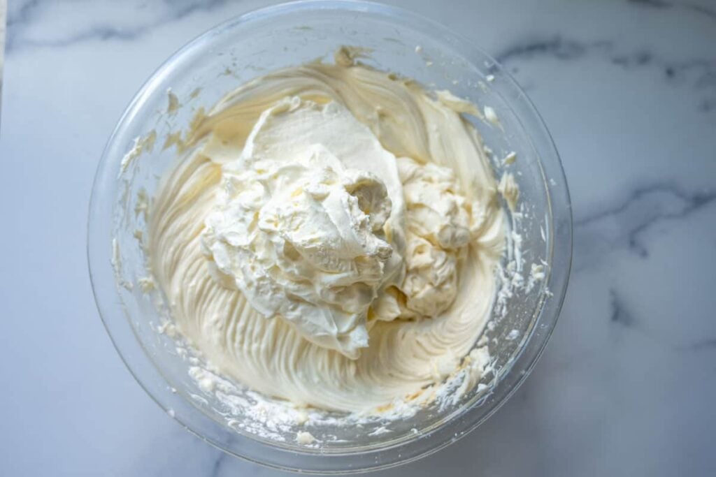 adding whipped cream into cheesecake filling in a glass bowl