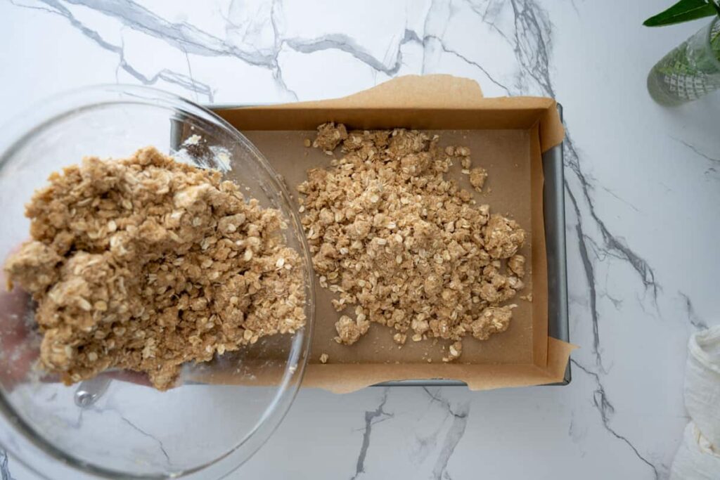 adding crumble mixture in a parchment lined pan