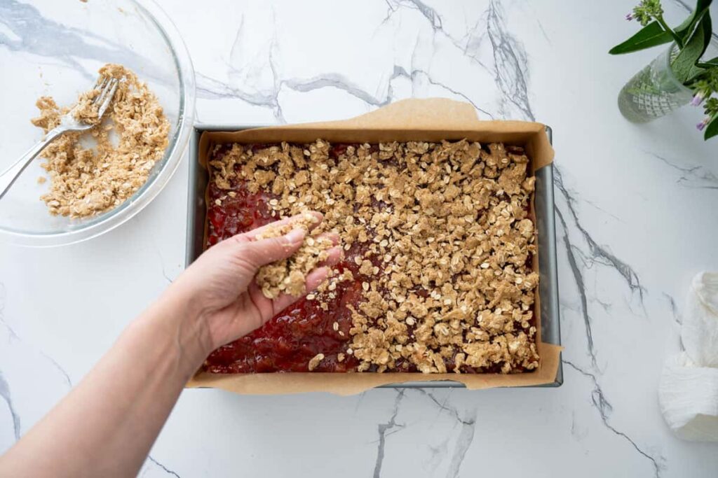 sprinkling the remaining crumble topping on rhubarb crumble bars