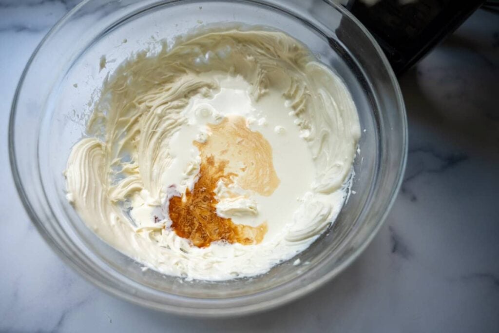adding heavy cream and vanilla extract to cream cheese