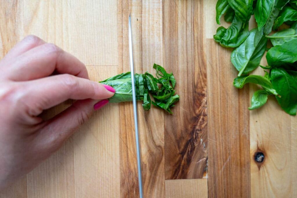 slicing rolled basil leaves into thin slices