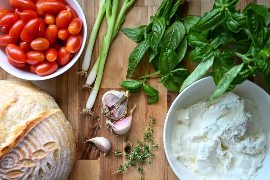 Herbed ricotta toast with marinated tomatoes ingredients on wooden board