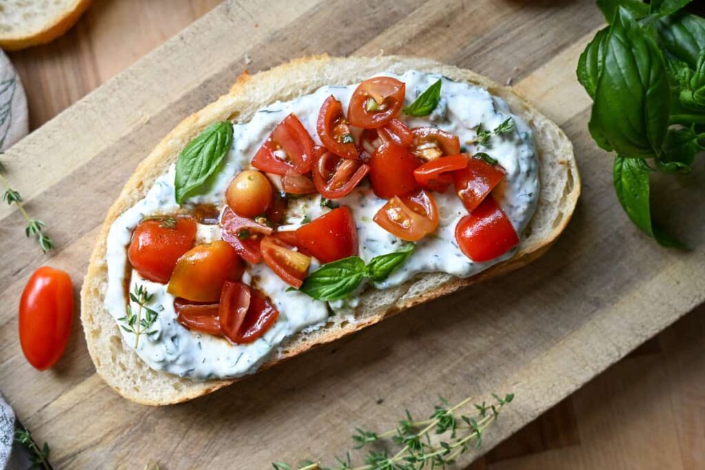 Herbed ricotta toast with marinated tomatoes on a wooden board