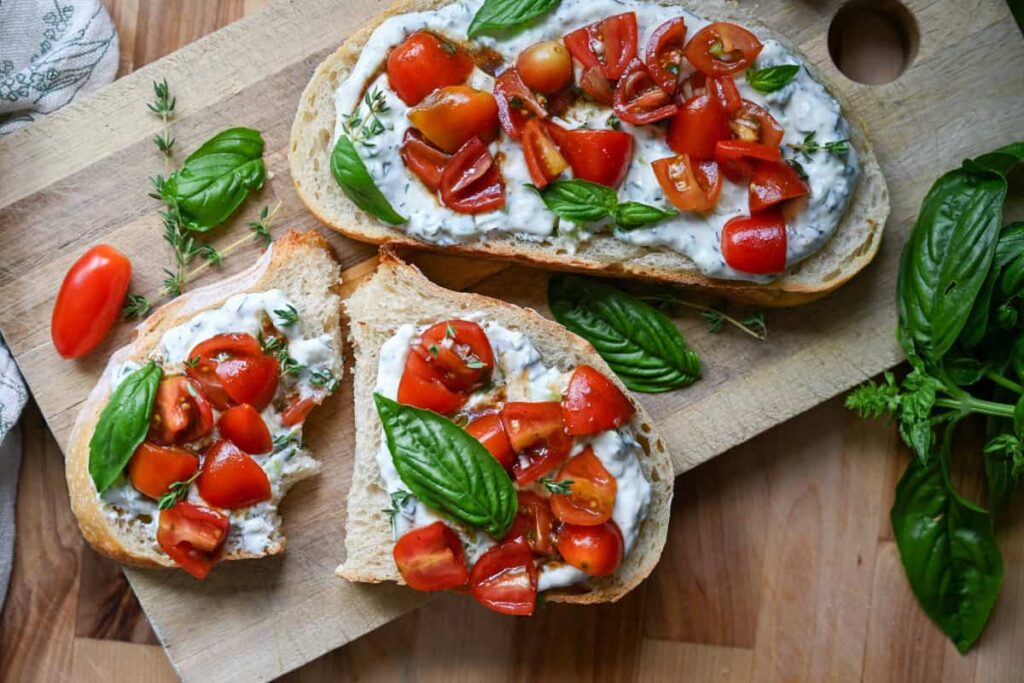 Herbed ricotta toast with marinated tomatoes on a wooden board