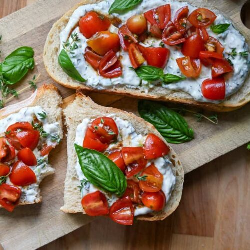 Herbed ricotta toast with marinated tomatoes on a wooden board