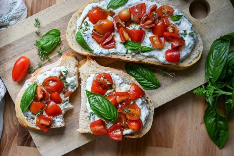 Herbed ricotta toast with marinated tomatoes on a wooden board