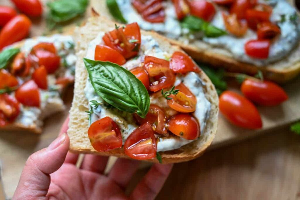 holding a piece of Herbed ricotta toast with marinated tomatoes