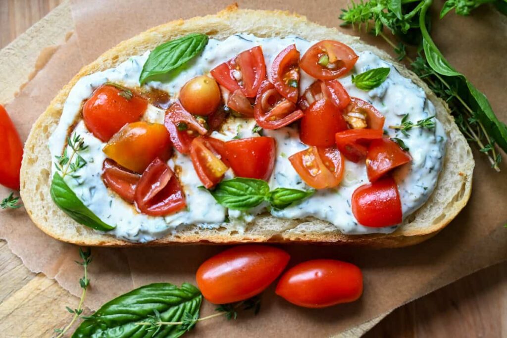 Herbed ricotta toast with marinated tomatoes on a wooden board
