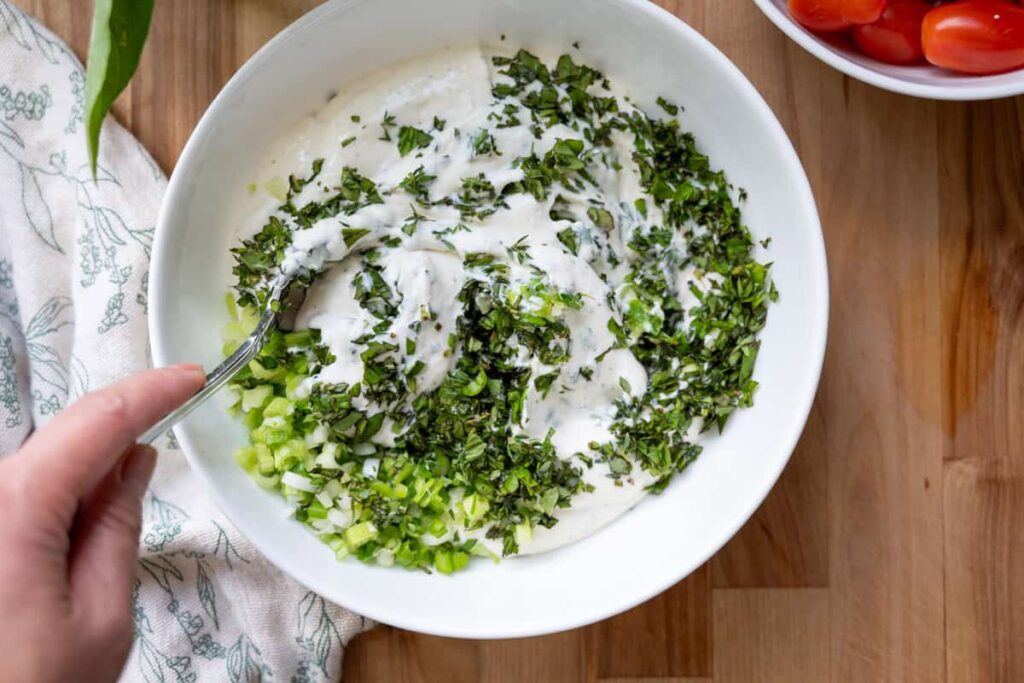 stirring herbs into whipped ricotta cheese in a white bowl