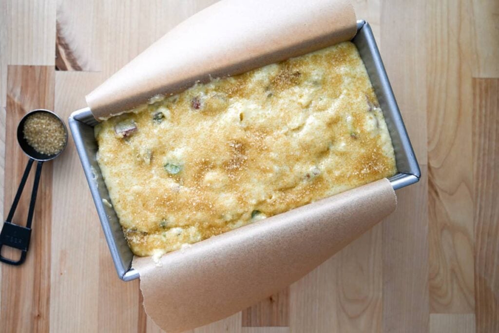 sourdough rhubarb bread batter in a loaf pan with turbinado sugar over the top of it
