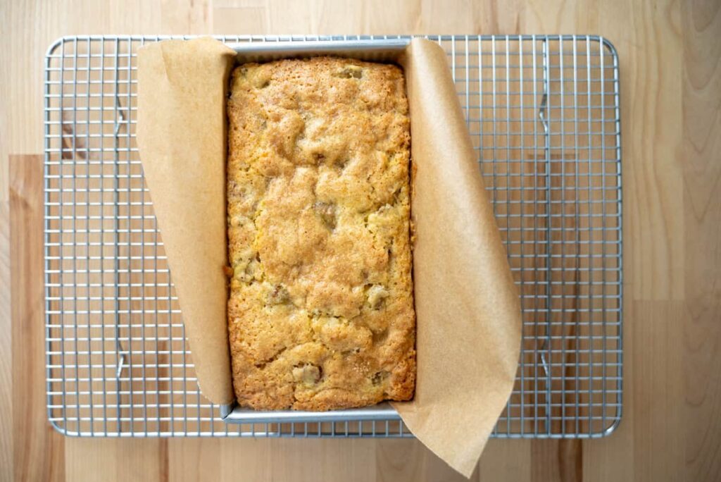 sourdough rhubarb bread in a loaf pan on a wire rack
