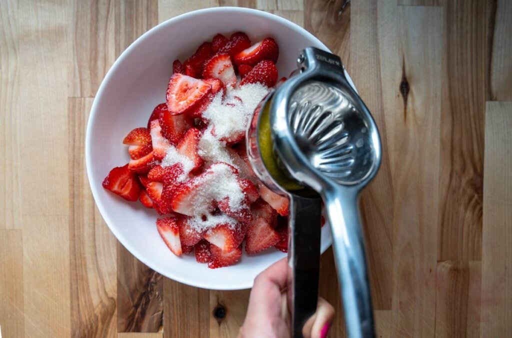 Macerating strawberries in a white bowl and adding a squeeze of fresh lemon