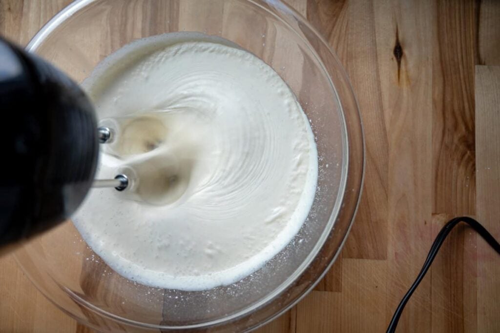 using a hand mixer to whip cream in a glass bowl