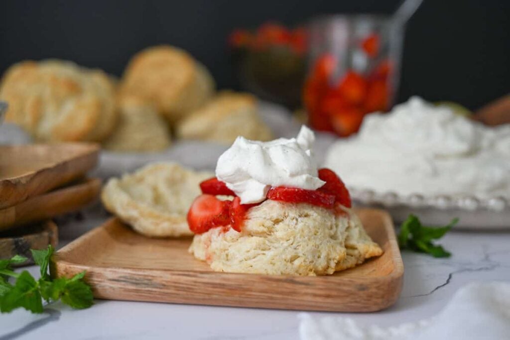 a sourdough biscuit with strawberries and whipped cream on a wood plate