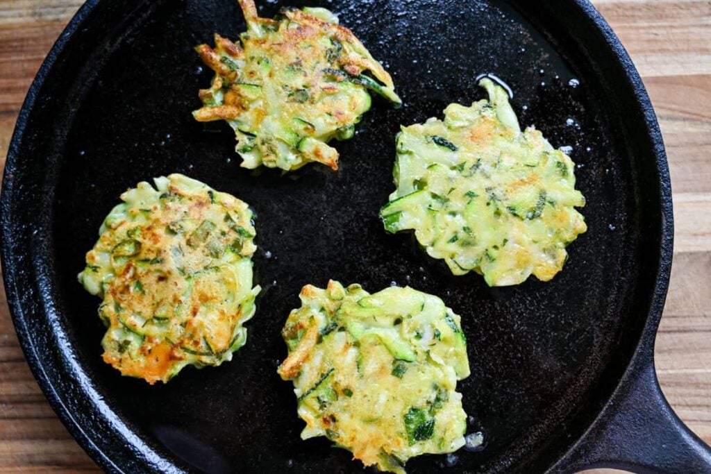 frying sourdough zucchini fritters in a cast iron pan