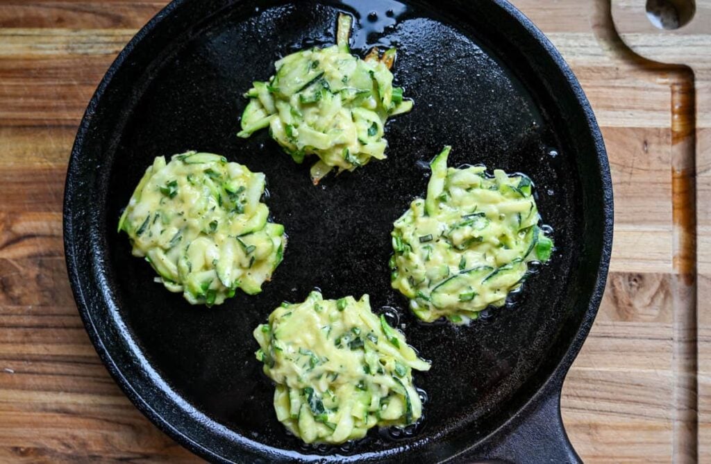 frying sourdough zucchini fritters in a cast iron pan