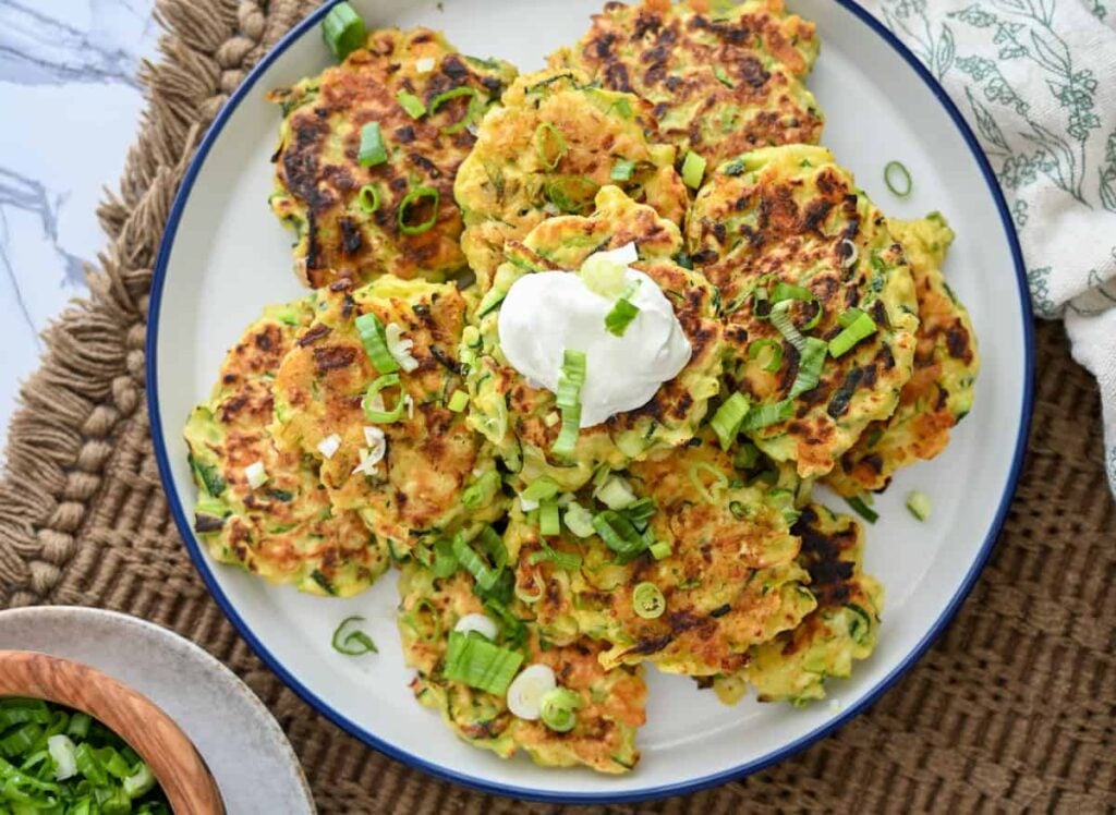 sourdough zucchini fritters on a plate with sour cream and diced green onions