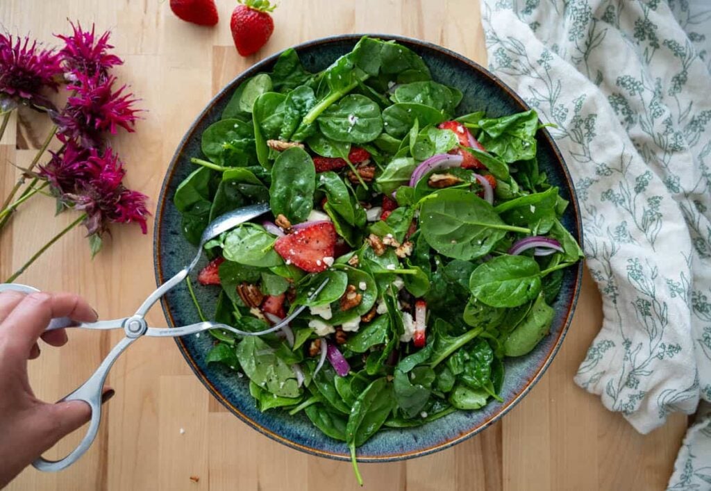 tossing strawberry spinach salad ingredients with salad dressing