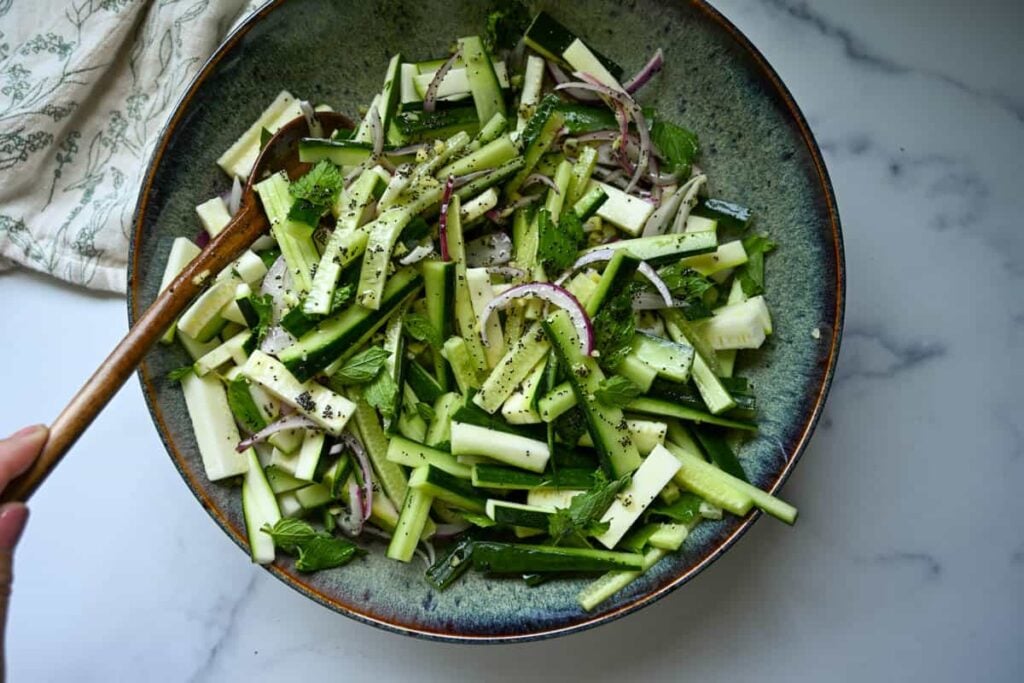 tossing the cucumber zucchini salad with a wooden spoon