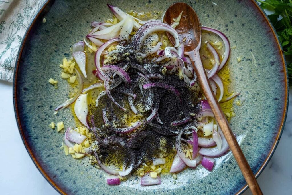 adding red onion slices and poopy seeds to the bowl