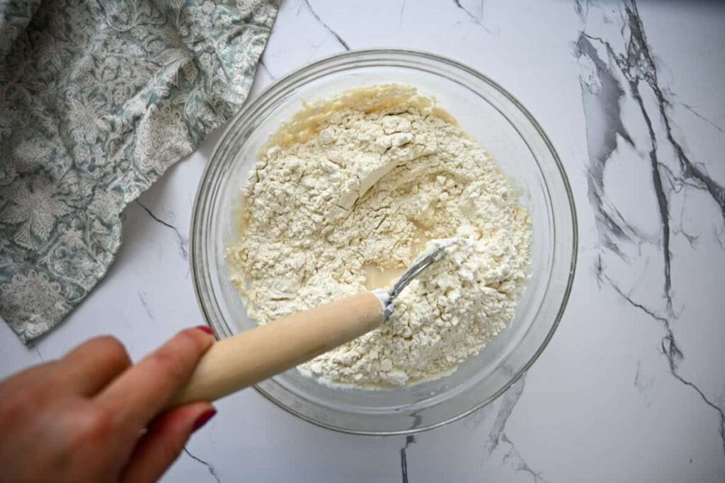 mixing sourdough ciabatta dough in a glass bowl with a dough whisk