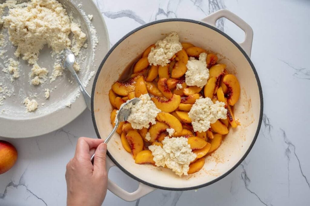 dropping sourdough biscuits over sliced peaches