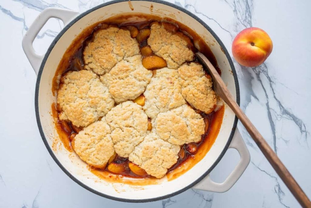 sourdough peach cobbler in a braiser with a wooden spoon