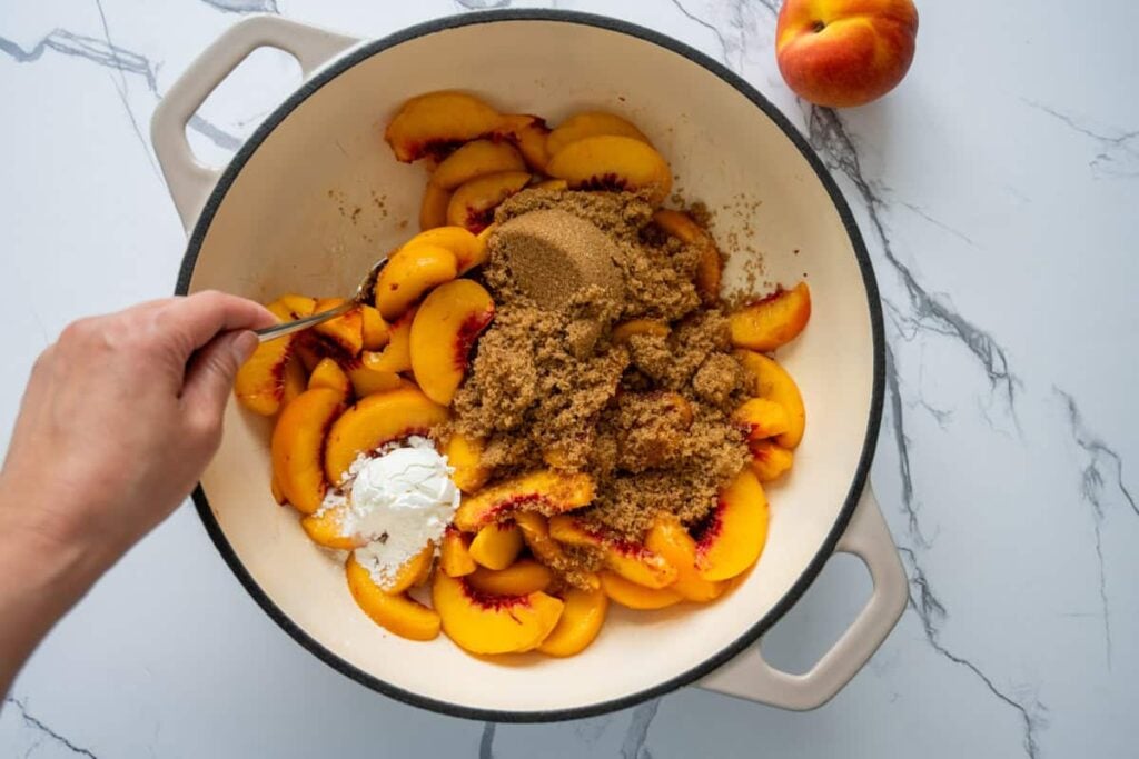 mixing peaches in braiser with sugar and other ingredients for peach cobbler 