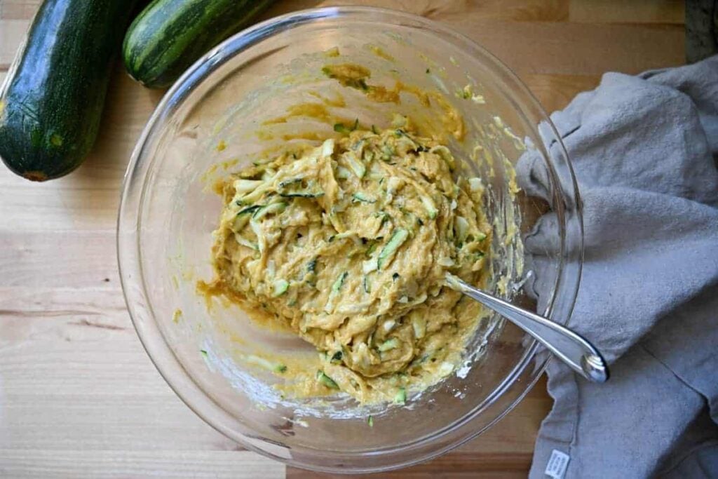 mixing sourdough zucchini muffins in a glass bowl