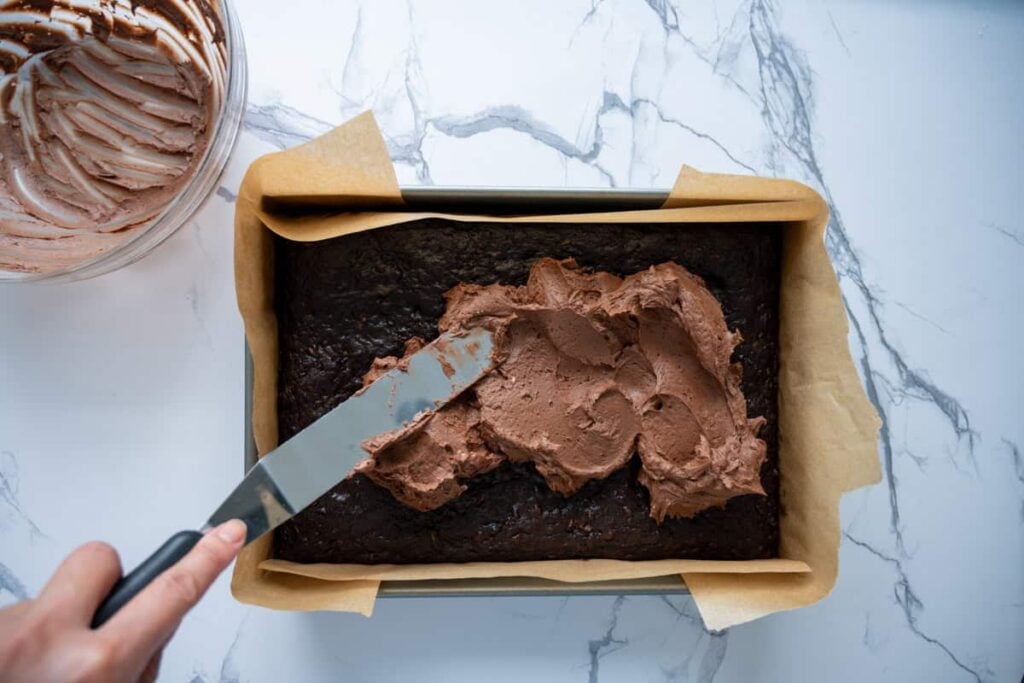 spreading chocolate frosting over the chocolate sourdough zucchini cake