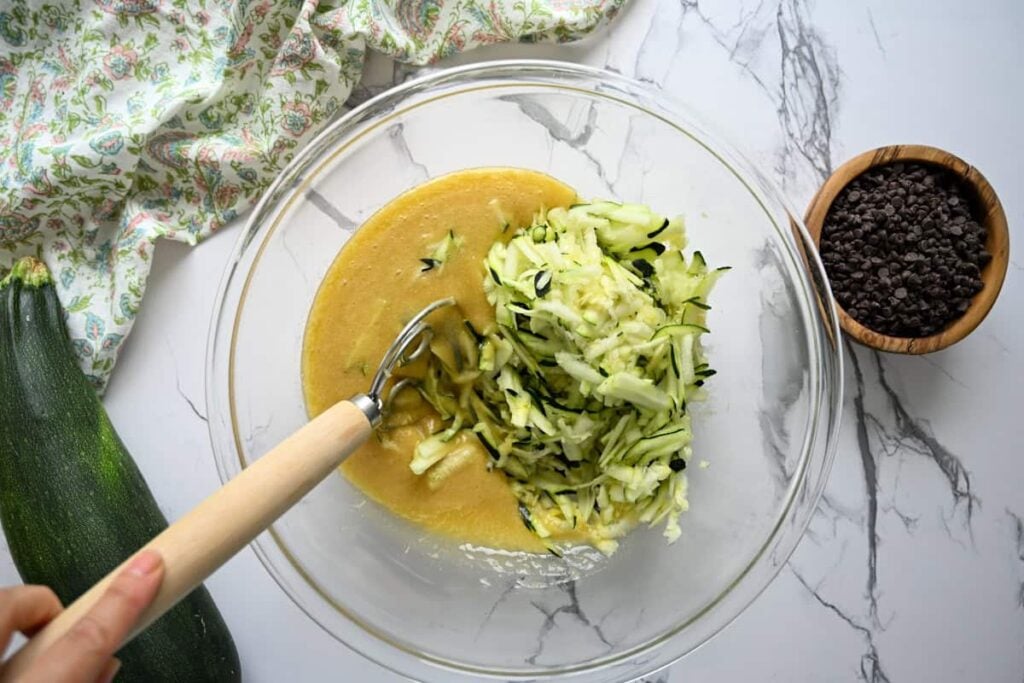adding shredded zucchini for chocolate sourdough zucchini cake in a glass bowl