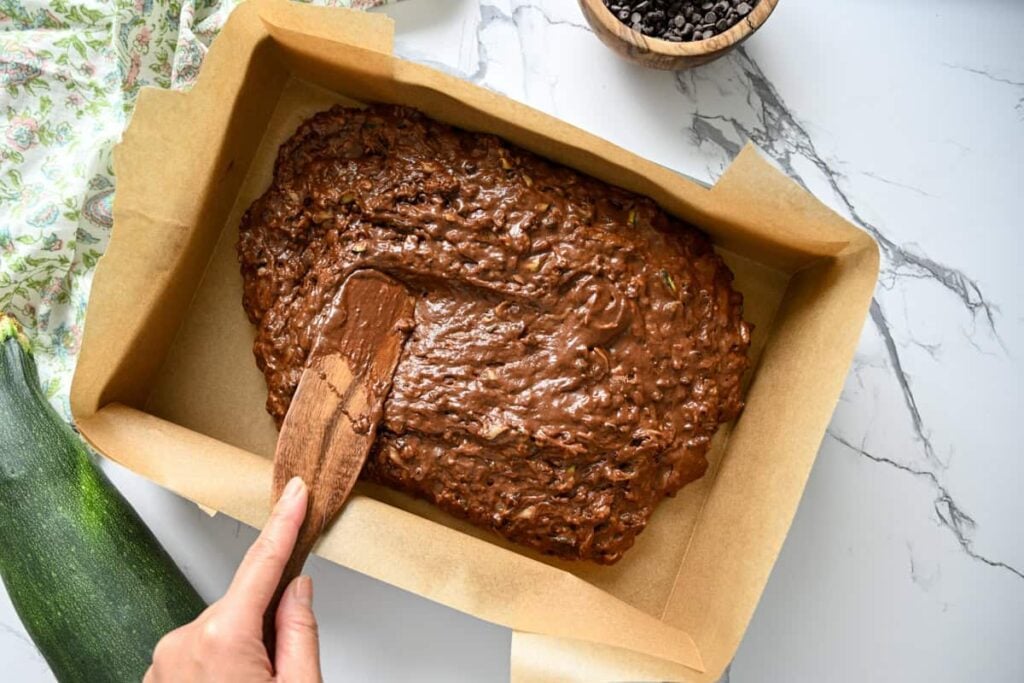 spreading the chocolate sourdough zucchini cake batter in a parchment lined cake pan