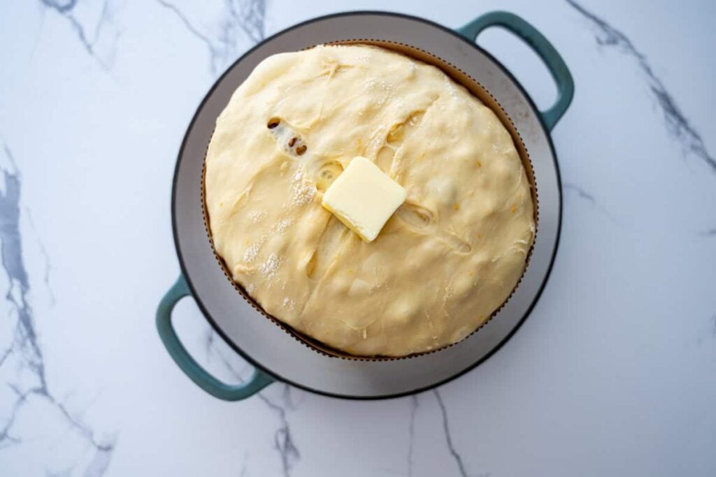 a proofed sourdough panettone bread in a paper mold with a pat of butter on top