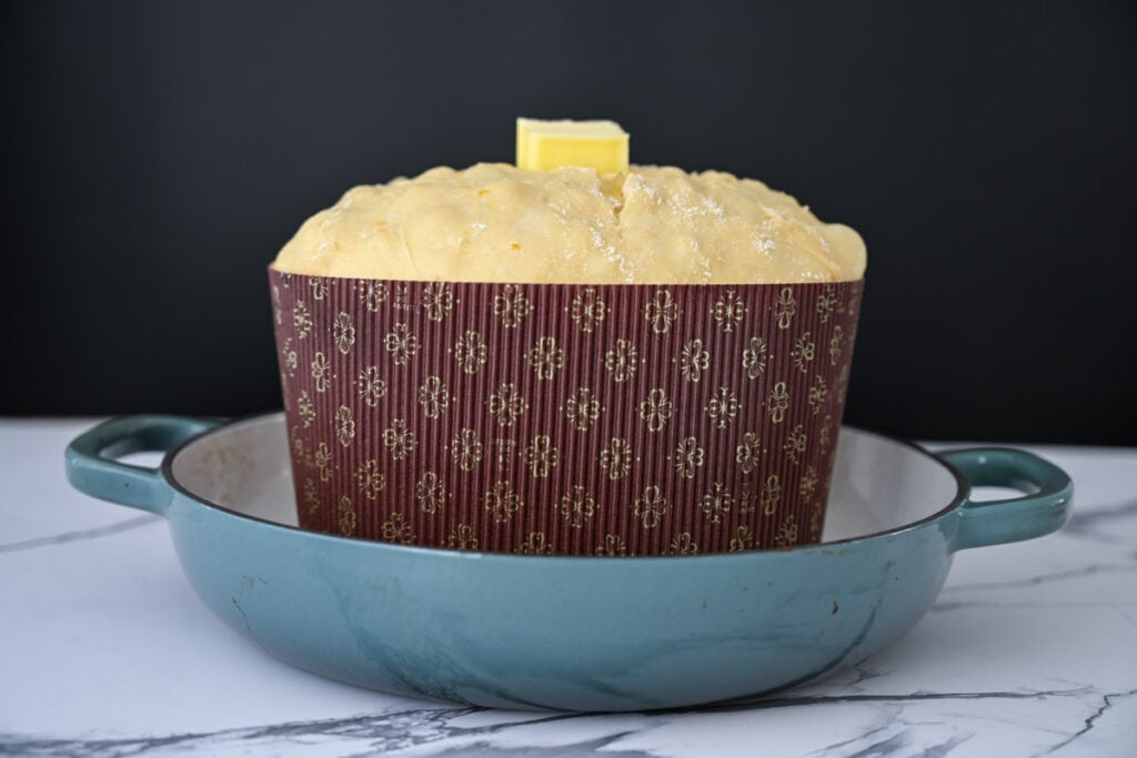 proofed sourdough panettone bread dough in a paper mold with a pat of butter on top